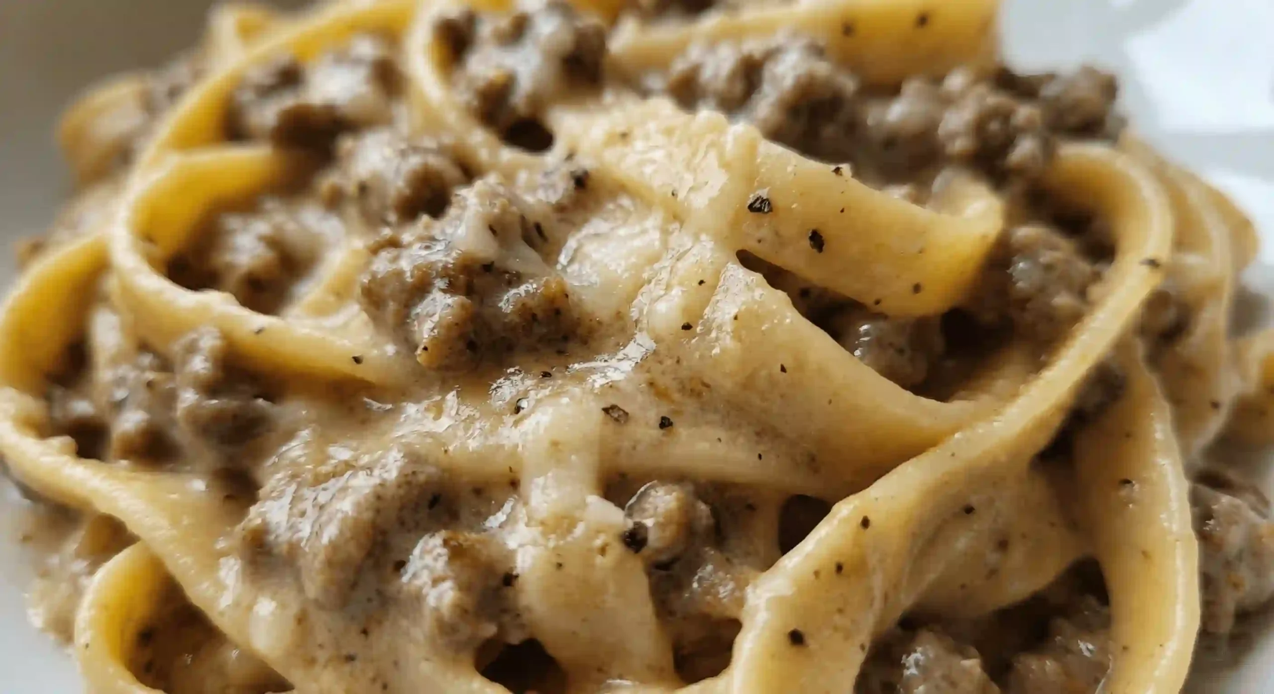 close-up of creamy beef and garlic butter pasta sauce coating wide ribbon pasta