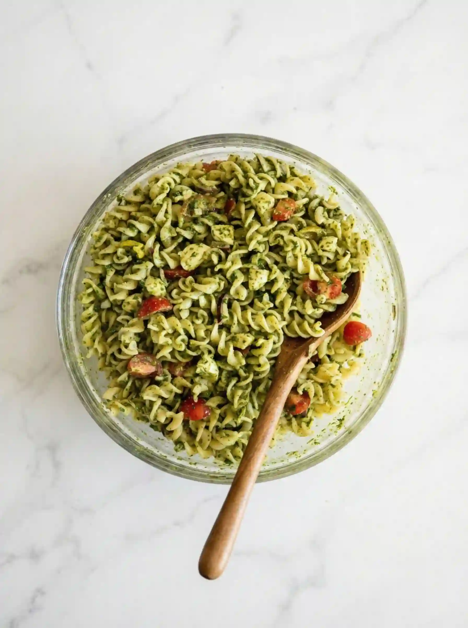 Pesto pasta salad with rotini, cherry tomatoes, mozzarella, and basil in a bowl