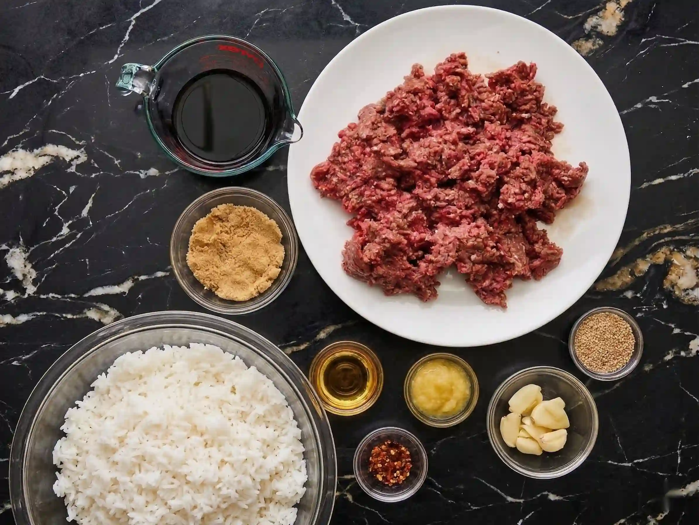 Ingredients for Korean ground beef bowl: beef, soy sauce, rice, garlic, brown sugar on black background