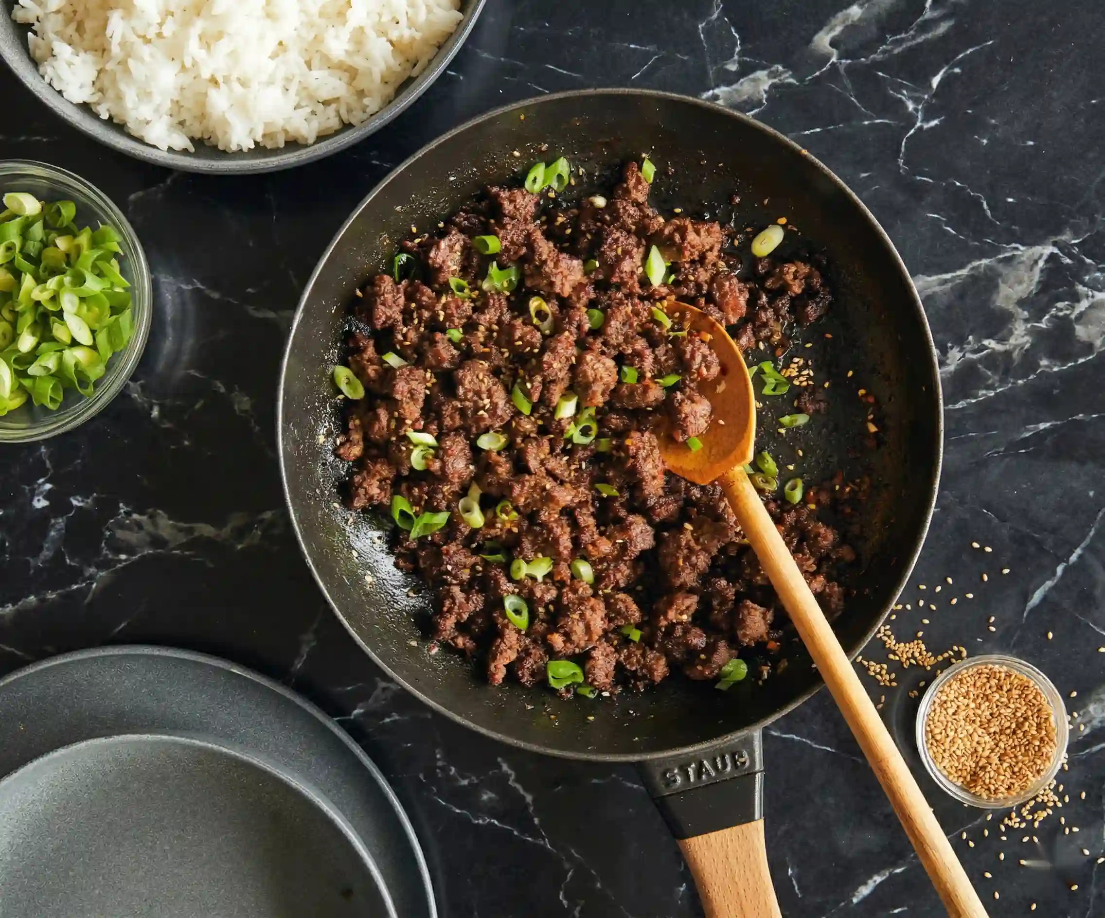 Ground beef cooking in skillet with green onions and wooden spoon for Korean beef bowl recipe