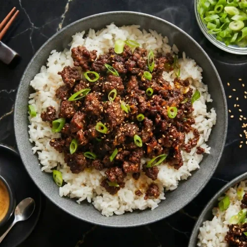 Ground beef cooking in skillet with green onions and wooden spoon for Korean beef bowl recipe