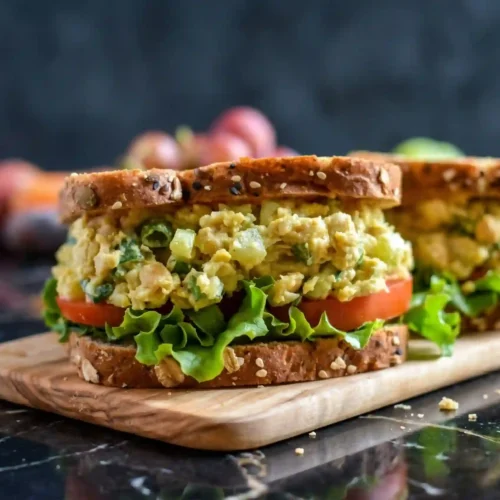 Vegan chickpea salad sandwich stacked on whole grain bread with lettuce and tomato