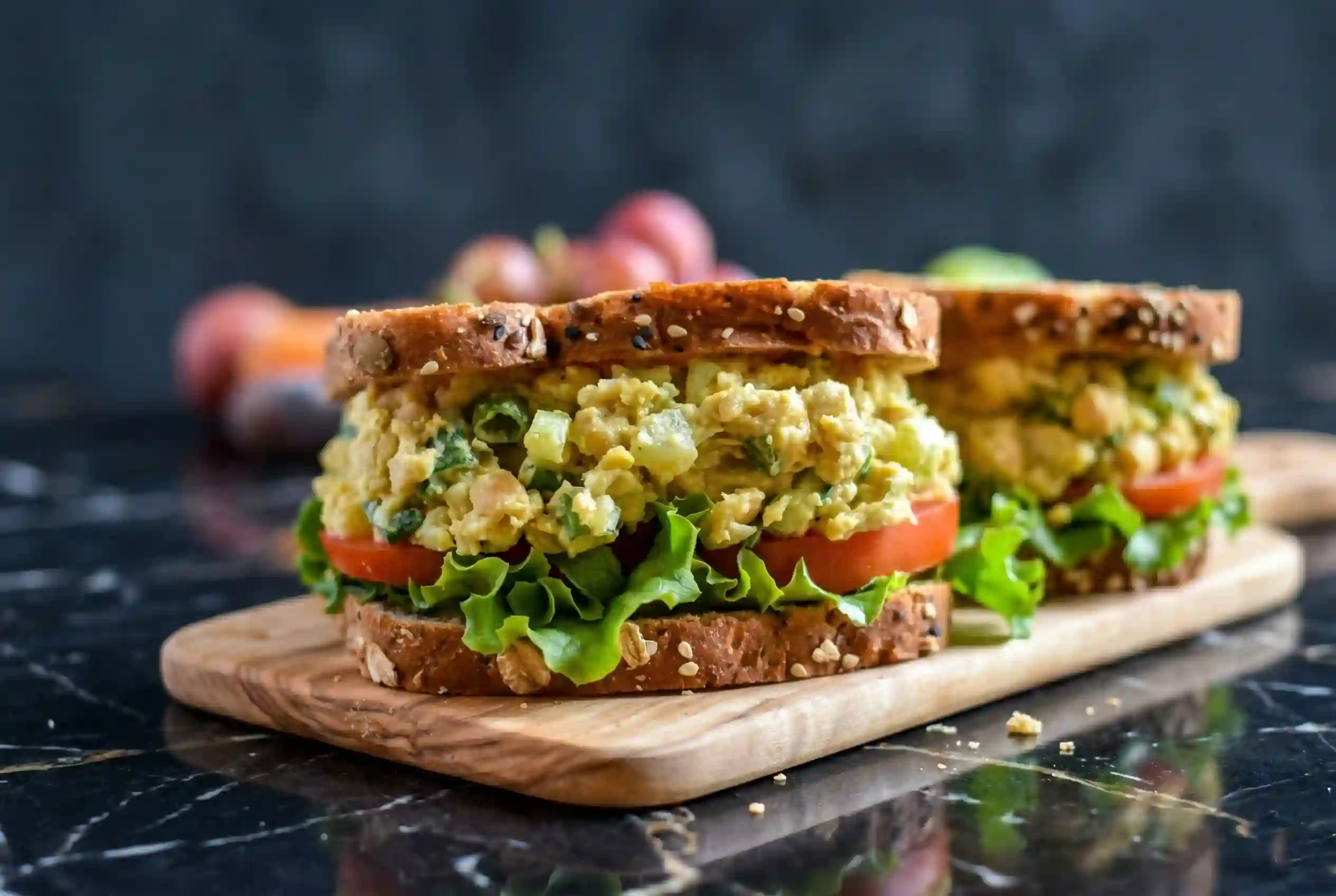 Vegan chickpea salad sandwich stacked on whole grain bread with lettuce and tomato