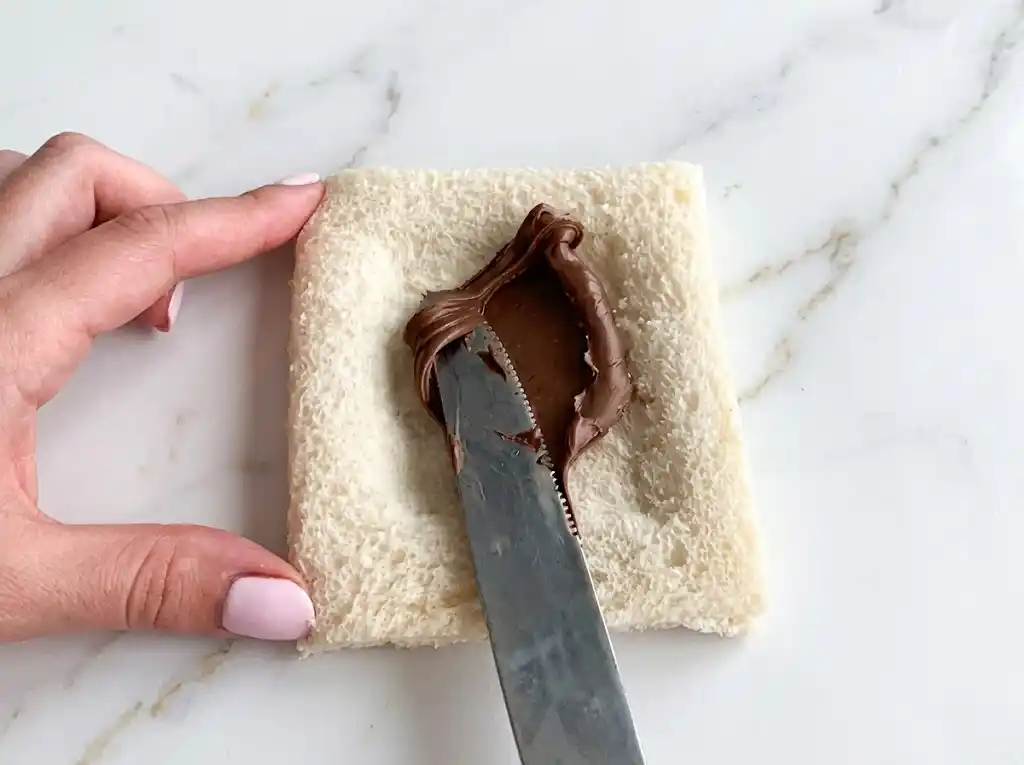 Spreading Nutella on white sandwich bread to make air fryer Nutella toast pies