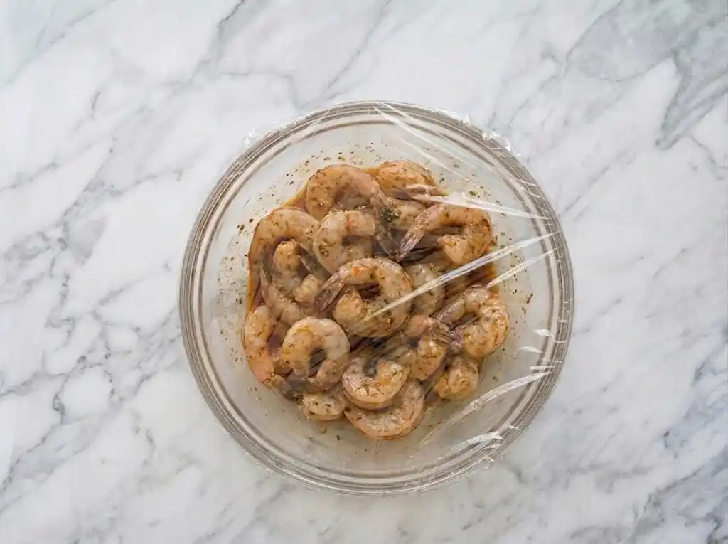 Marinate A bowl of coated raw shrimp resting in marinade before being assembled into Grilled Shrimp Skewers.