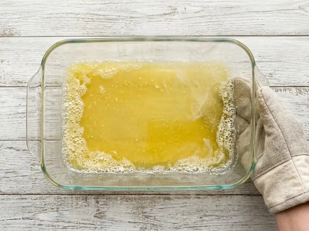 canned peach cobbler cheese Melted butter sizzling in a 9x13 baking dish for the first step of an easy canned peach cobbler recipe.