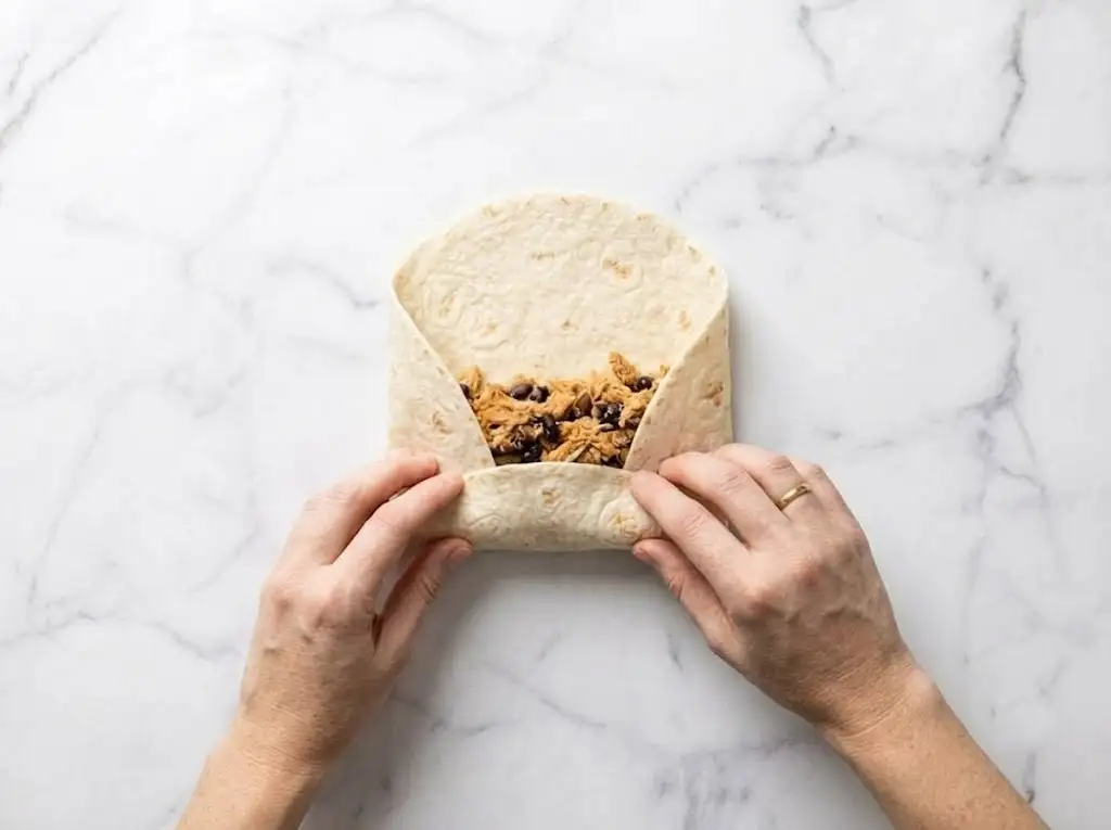 Rolling a Chicken Caesar Wrap tightly with the filling tucked inside.