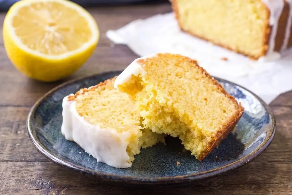 A whole glazed Starbucks lemon pound cake recipe resting on a marble surface surrounded by fresh lemons, showcasing a vibrant and better than Starbucks lemon loaf.
