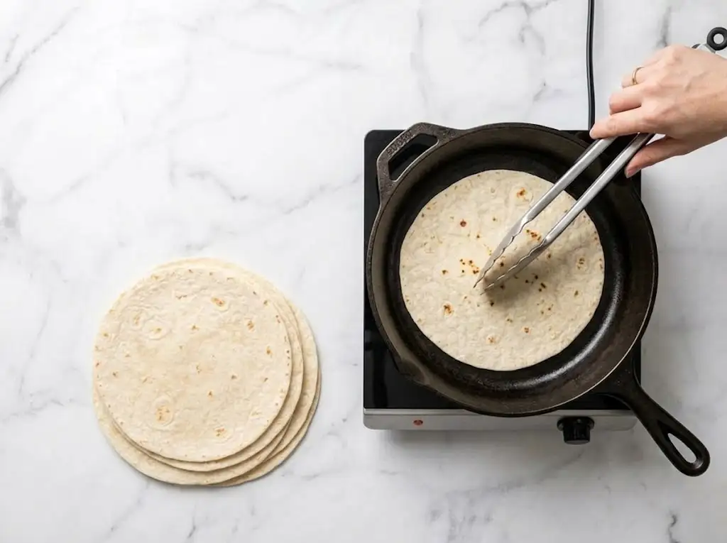 Warming flour tortillas in a skillet before assembling a Chicken Caesar Wrap.
