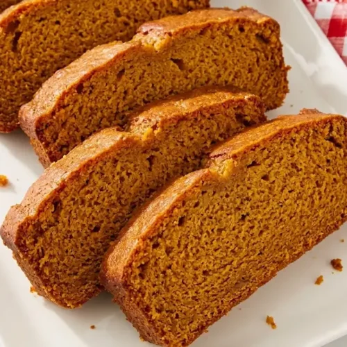 A close-up shot of freshly sliced, golden-brown Moist Pumpkin Bread served on a plate with red and white checkered napkins, ready to enjoy.
