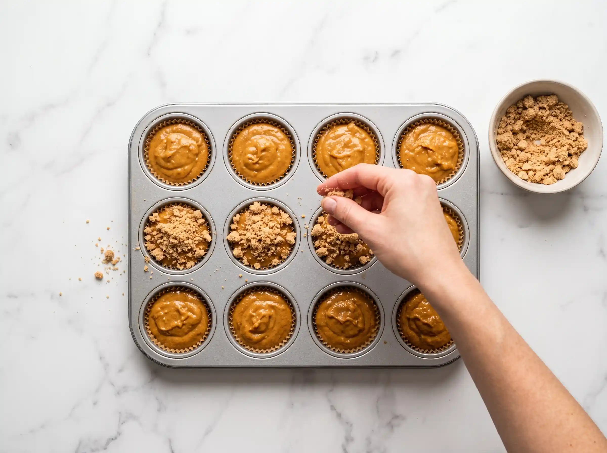 A person uses a toothpick to gently swirl the cream cheese filling into the pumpkin batter for the pumpkin cream cheese muffins.