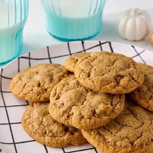 A close-up stack of fresh, chewy Pumpkin Snickerdoodle Cookies coated in cinnamon sugar on a rustic plate.