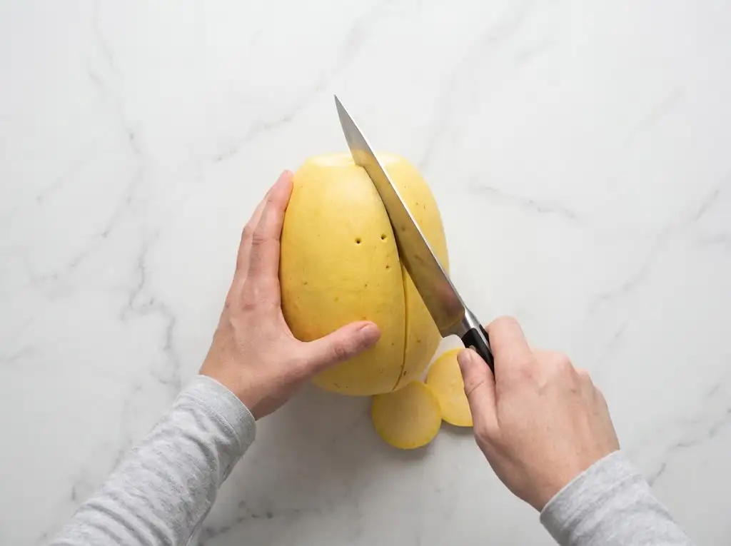 STEP2 Air Fryer Spaghetti Squash Step 2 of making air fryer spaghetti squash: hands slicing a raw squash in half lengthwise with a chef's knife.