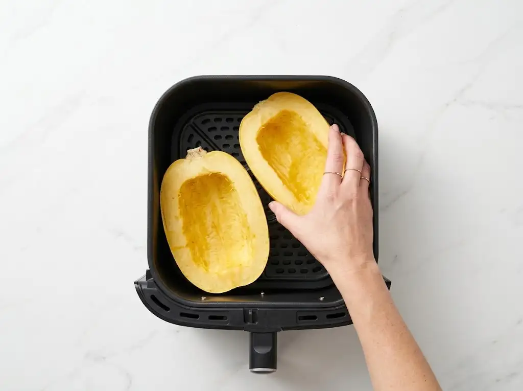STEP5 Air Fryer Spaghetti Squash Step 5 of making air fryer spaghetti squash: placing the prepared squash halves into a black air fryer basket.
