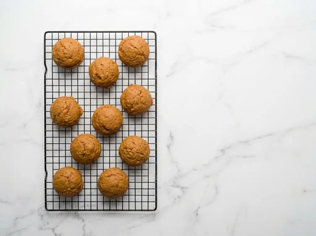 STEP8 Pumpkin Cookies with Cream Cheese Frosting "A batch of freshly baked pumpkin cookies cooling on a wire rack on a kitchen counter."