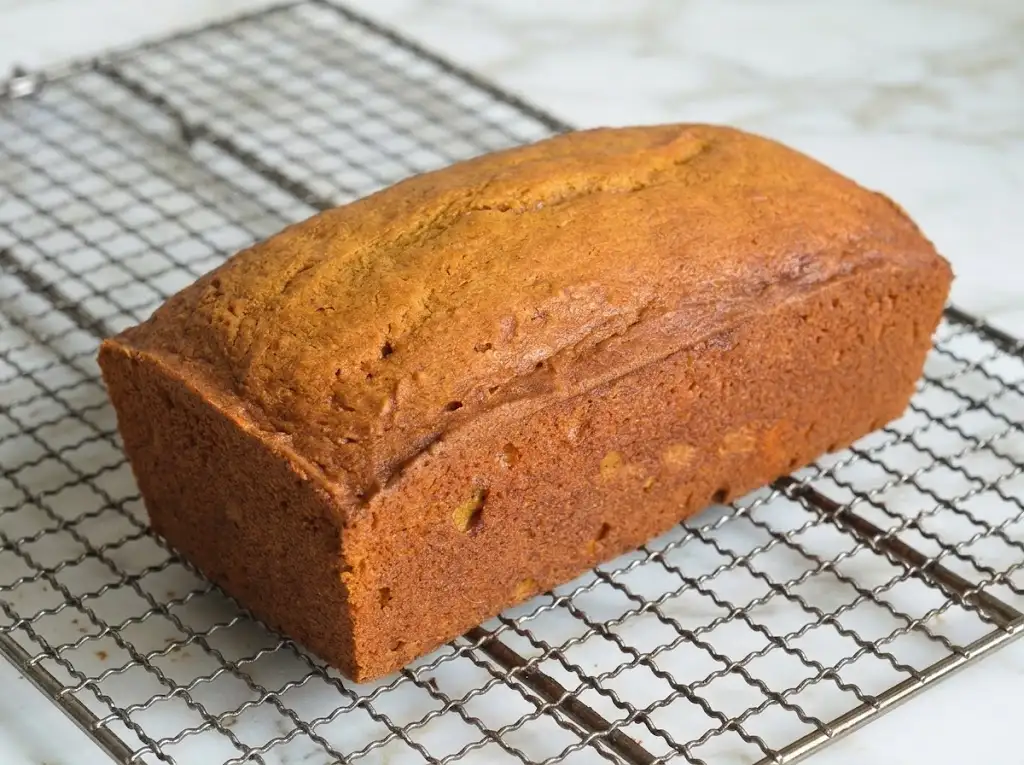 STEP9 Moist Pumpkin Bread Hands carefully lift the completed, cooled loaf of Moist Pumpkin Bread from the wire cooling rack using the parchment paper overhangs.