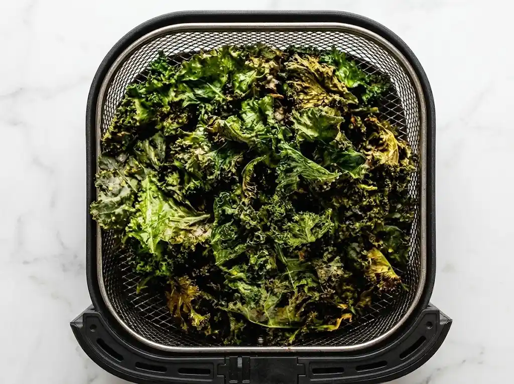 Freshly cooked and crispy air fryer kale chips resting inside a black air fryer basket on a white countertop